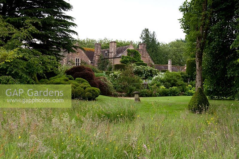 Cothay Manor, Greenham, Somerset. House in distance with long grass, trees and shrubs 