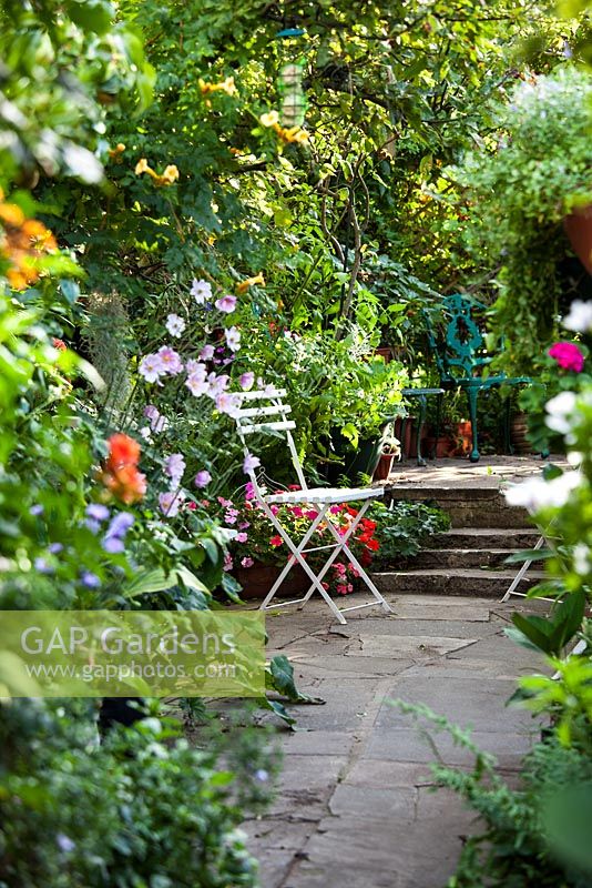 Stone path leading to white french chair and stone steps with Anemone and late summer border