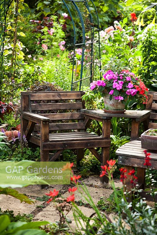 Wooden chair on stone floor with Bergonias on side table and Schizostylis coccinea 'Major'
