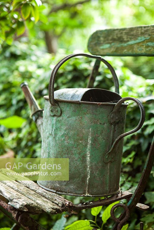 Rusty old watering can on old french chair, London, July