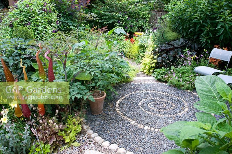 Spiral reflexology design made of pebbles, surrounded by summer borders. 