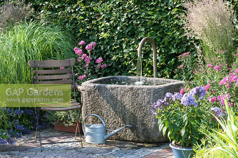 Stone trough water feature, chair and mixed planting including Malva moschata, Phlox 'Laura' and Nepeta