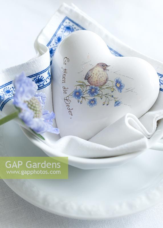 Decorative ceramic heart bedded on napkin in a bowl with Scabiosa blossom