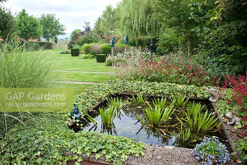 View over the small pond and planting. Miscanthus sinensis 'Morning Light',  Stratiotes aloides, Persicaria amplexicaulis 'Firedance', Persicaria amplexicaulis 'Alba' Bistort. Tuin de Villa