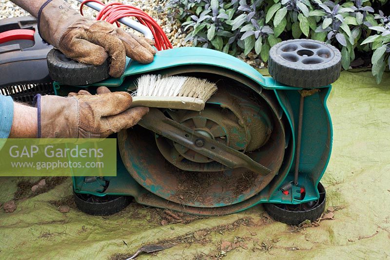 Cleaning a small, electric lawnmower after use - a groundsheet is used to collect debris.