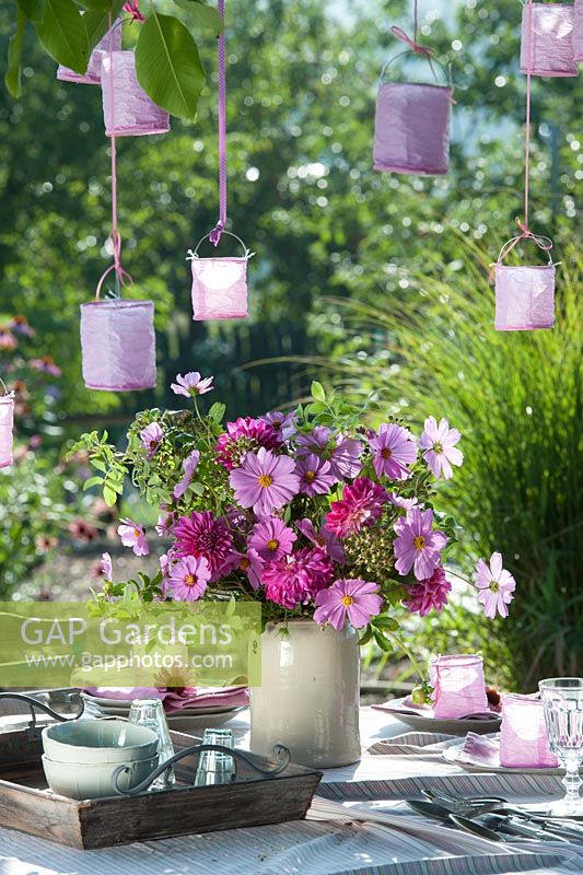 Display of Cosmea, dahlias and small rose hips with lanterns hanging from tree