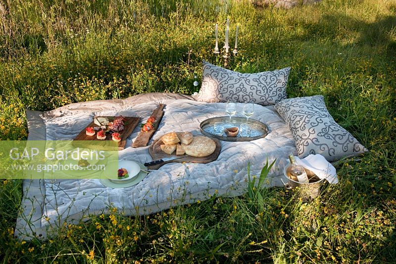 Picnic in a meadow on a soft blanket with cushions, candles, fruit, cheeses, fresh bread, cured meats and wine in glasses at Borgo Santo Pietro, Tuscany, Italy