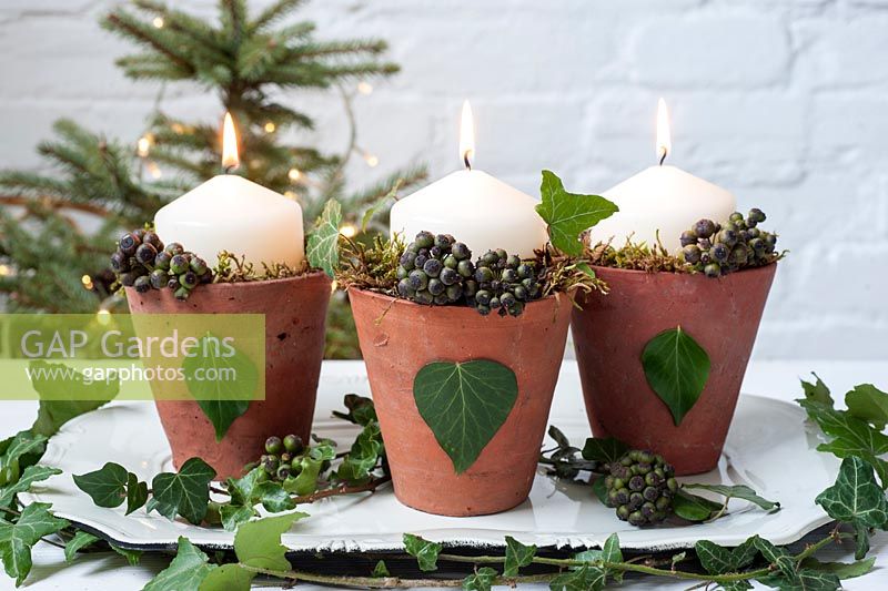 Candles in decorated terracotta pots with hedera helix leaves and berries - ivy and moss