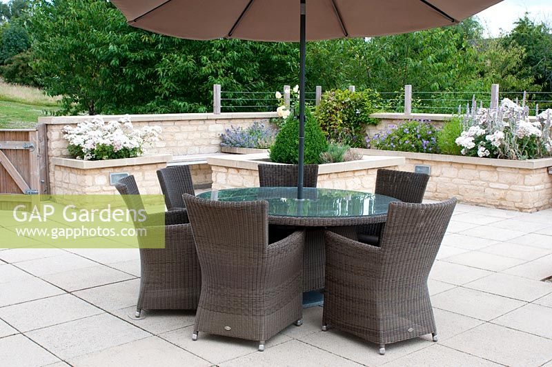 Patio with ratten chairs table and parasol and cotswold stone raised beds  - part of the landscaped gardens of a retirement village