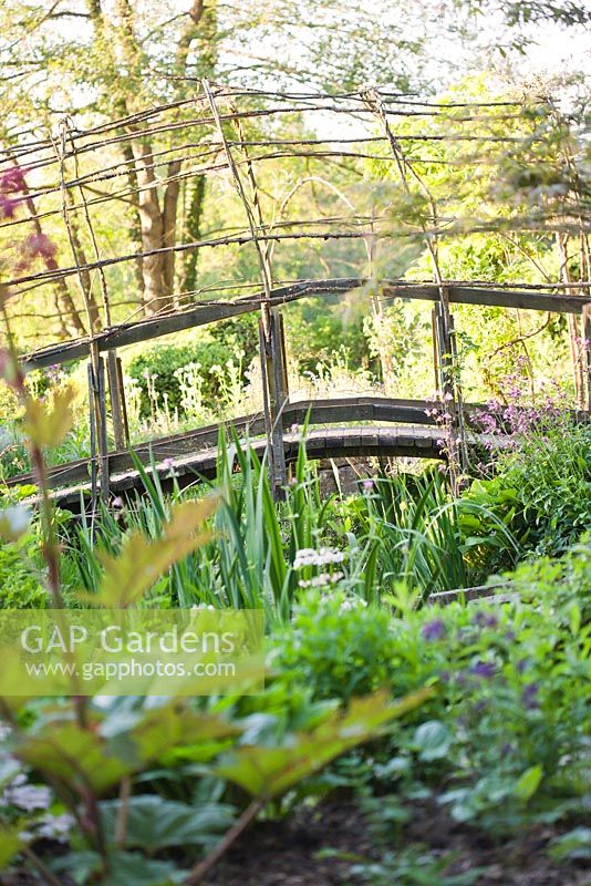 Naturalistic woven style arched bridge over  pond in early summer