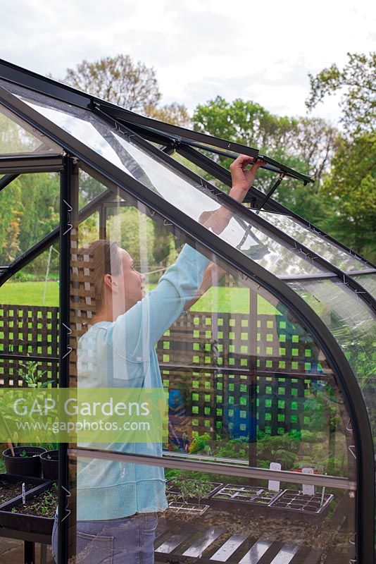 Woman opening windows in a greenhouse.