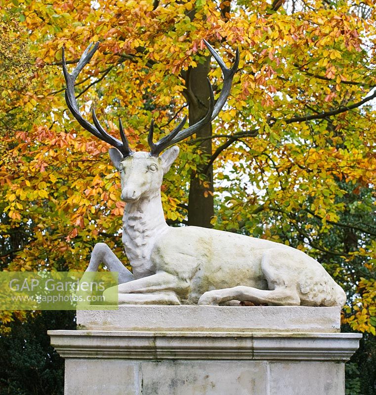 A stone stag sculpture at the east end of cross walk surrounded by autumn colour. Saling Hall, Essex