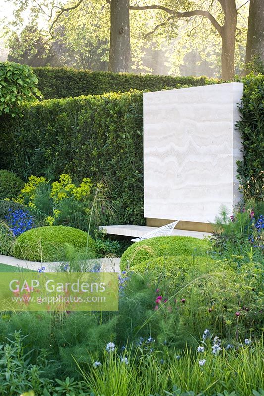 The Telegraph Garden, RHS Chelsea Flower Show 2014, gold medal winner. View across Italianate garden to stone wall panel in boundary hedge.  Buxus sempervirens,  Tilia x Europea 'Pallida'