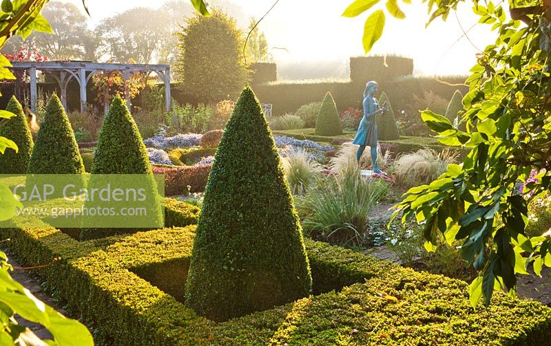 The hedged in formal garden at dawn with box and berberis hedging and topiary - girl statue called the 'lamp of wisdom'