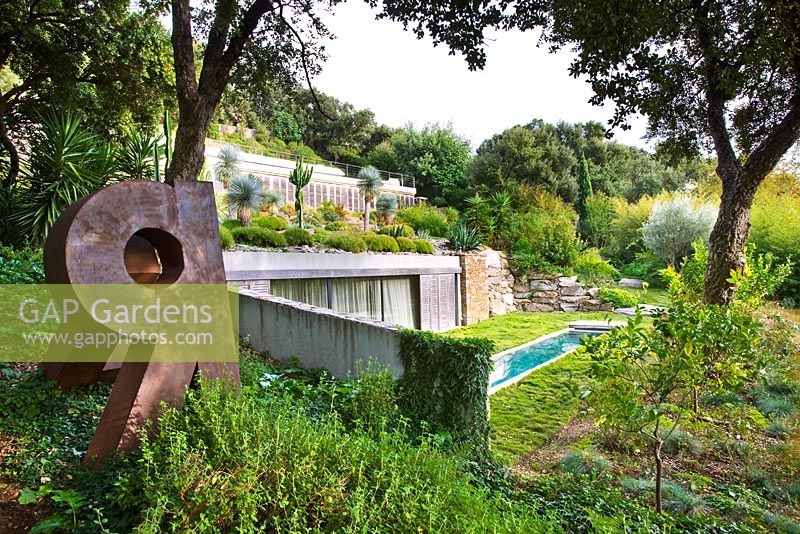 Pool house with lawn, swimming pool and succulents growing on the roof. Metal sculpture in foreground. Designer: Jean-Laurent Felizia, France