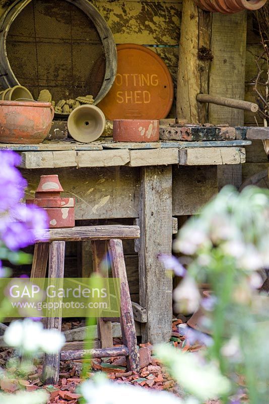 View to a vintage potting bench with various tools and broken terracotta path.  Dial A Flight, RHS Chelsea Flower Show 2014. 