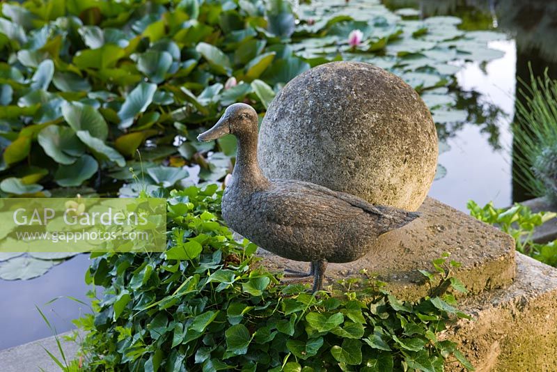 The waterlily pond from the gravel terrace beside the house - duck sculpture and stone ball. Les Confines, Provence, France
