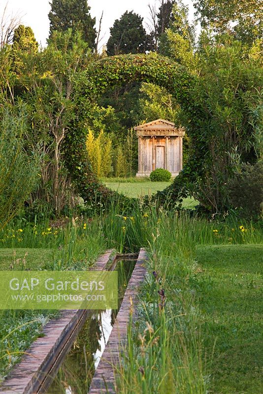 Water rill leads out through an arch hedge with view to folly. Les Confines, Provence, France