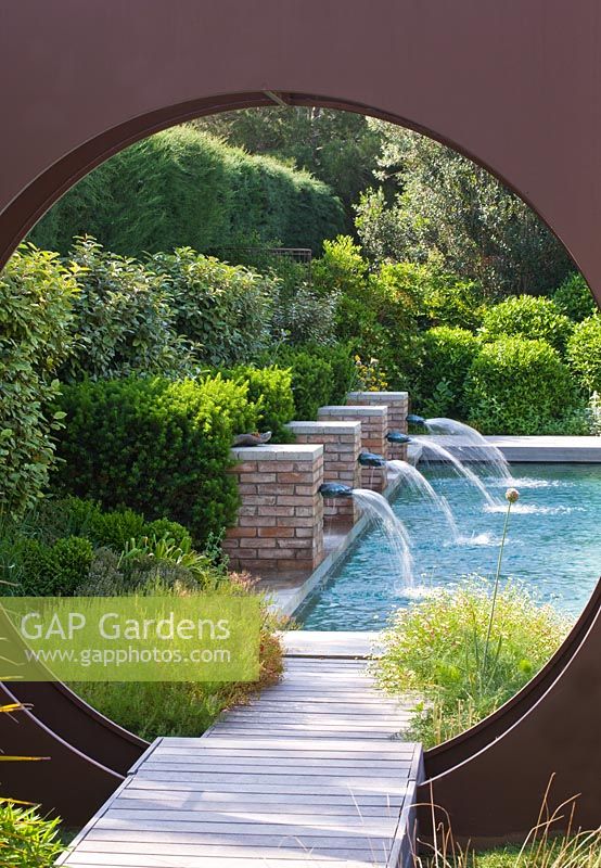 Modern contemporary garden - metal 'oculus' circle and swimming pool beyond with four brick water spouts