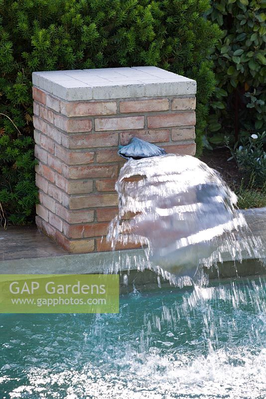 Brick backed water spout spraying water into swimming pool 