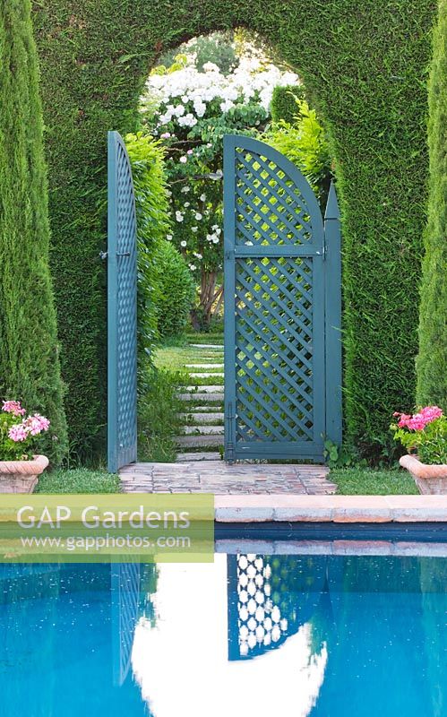 Swimming pool in portuguese garden and view through hedge and blue trellis gate. Les Confines, Provence, France
