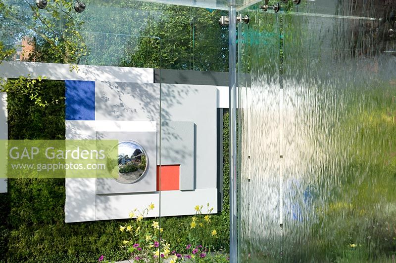The Mind's Eye Garden One wall of a glass box building with water cascades. Looking towards green living wall with geometric artwork relief with convex mirror. 