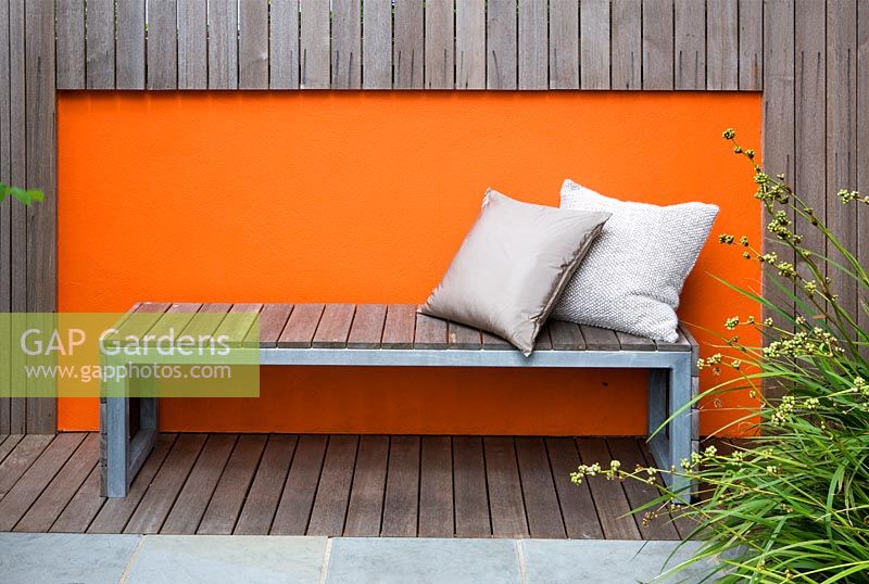 Modern contemporary garden in Brighton with decking, orange panels on walls, Wooden bench and cushions