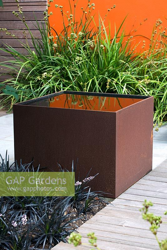 Modern contemporary garden in Brighton with square metal water feature on decking with wooden panel walls and orange panel 
