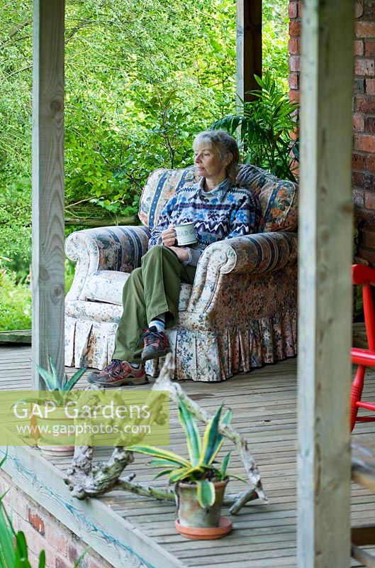 Ros Bissel sitting on an armchair on her veranda. Moors meadow garden and nursery, Herefordshire