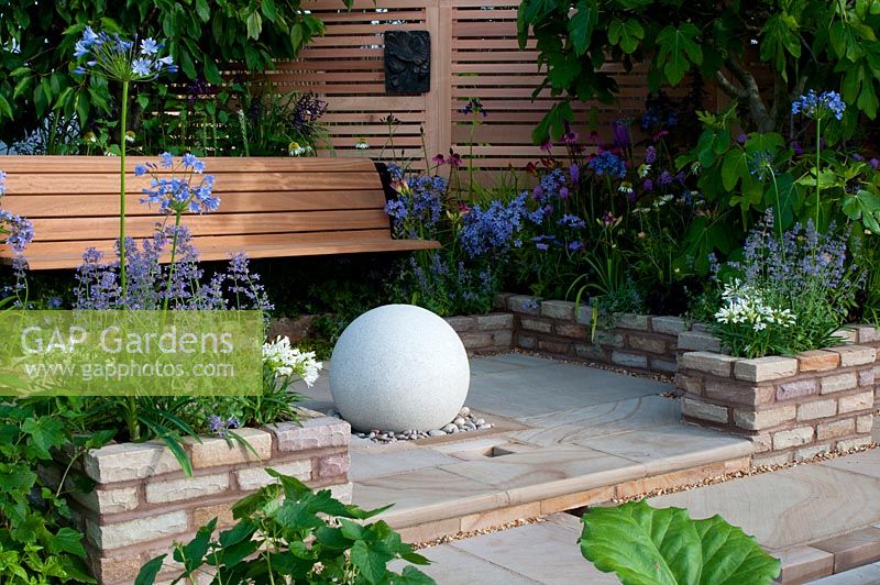Wooden bench and wall with stone sphere feature on patio in The Edible Medley Show Garden at RHS Tatton Flower Show 2013