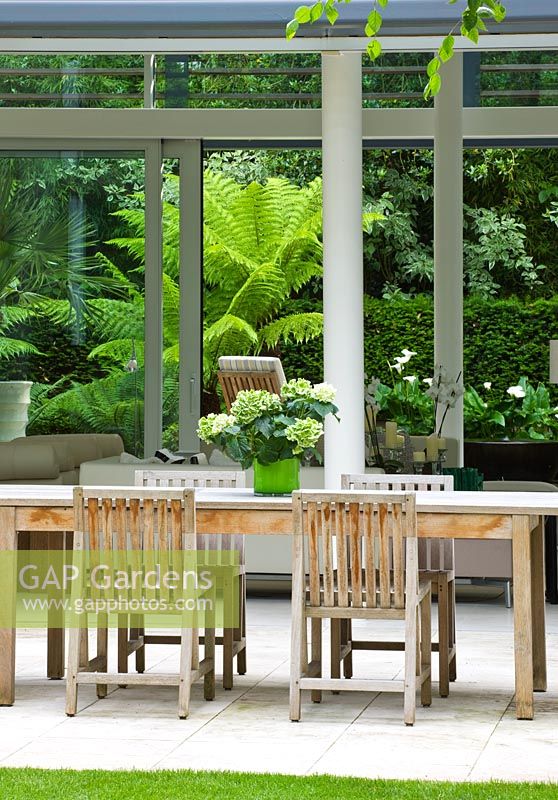 Limestone patio, table and chairs, view through glass pavilion to tree fern garden - The Glass House - Architects Terry Farrell Partners - Garden design by Sallis Chandler
