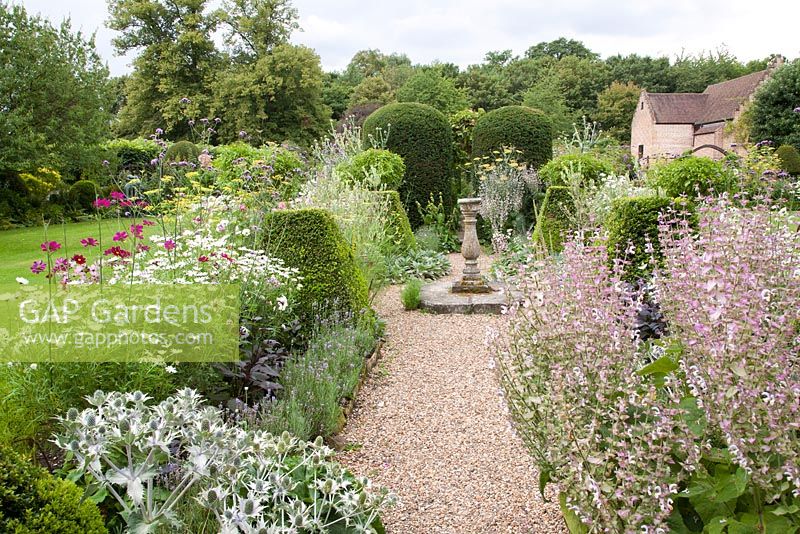 Mixed Cosmos, Leucanthemum, Fennel, Verbena, Eryngium, Salvia and clipped topiary in summer border with stone sundial. Chenies Manor, Buckinghamshire