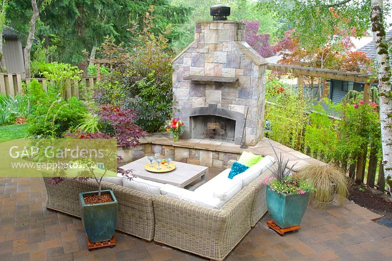 Outdoor lounge with sectional sofa, coffee table and fireplace. Teal ceramic pots planted with Acer palmatum - Japanese Maple and annual flowers.