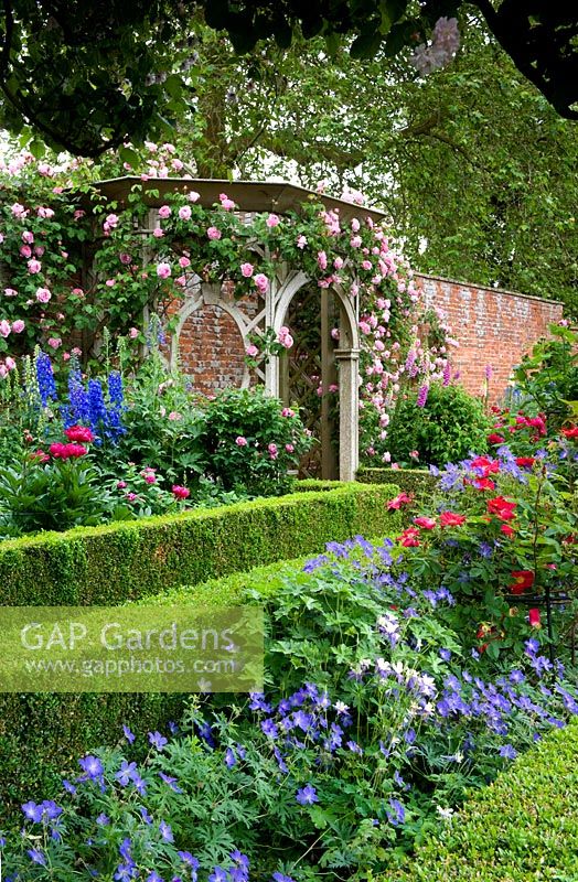 A classic English walled garden with box edged ornamental borders, climbing roses and wooden ornamental arbour. Seend, Wiltshire