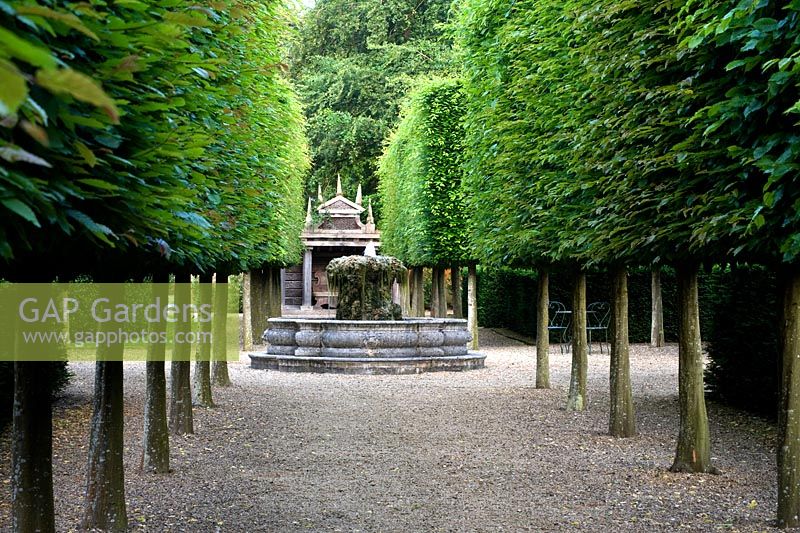 French-style allee of pleached lime leading through axis of garden with central ornate water feature and wooden pavilion at the far end. Seend, Wiltshire