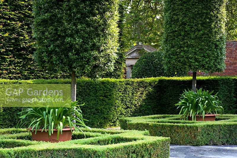 Italianate topiary garden with stone gate pediment glimpsed between hedges. Seend, Wiltshire