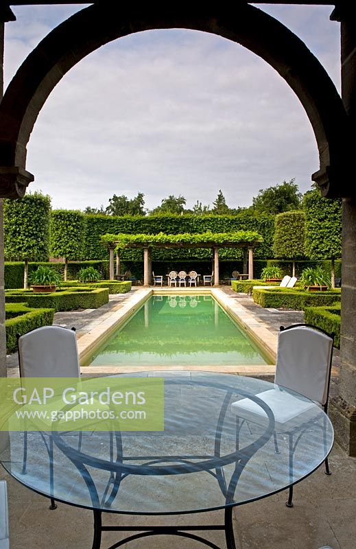 Italinate garden viewed from under loggia with glass table and canal-like swimming pool. Seend, Wiltshire