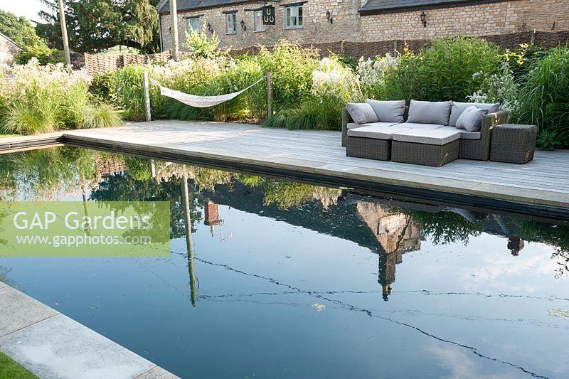 Pool garden with swimming pond, deck, hammocks and seating surrounded by naturalistic planting. Old Rectory, Batcombe, Somerset, UK