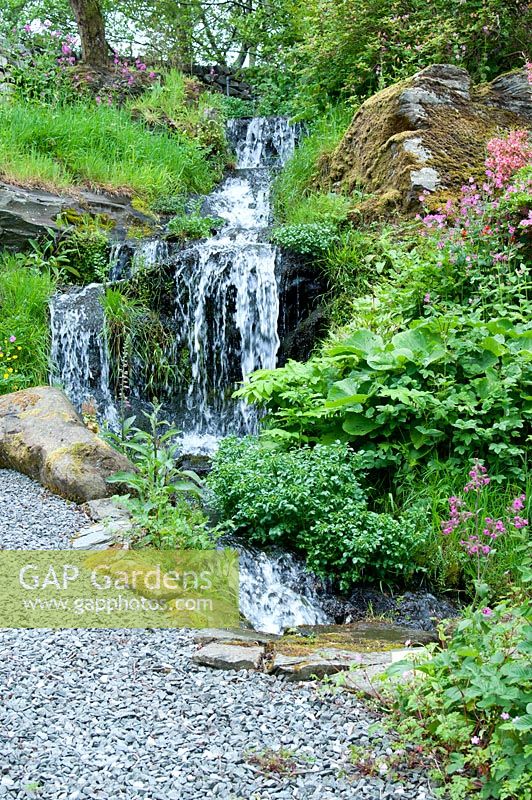 Waterfall cascading down in wild area of garden by gravel path