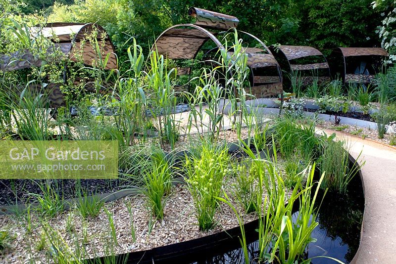 Title: Le Jardin Dechene. Pergolas made of a construction of metal hoops. Borders in plateaus planted with  Arundo donax and in the oval shaped pools aquatic plants like Menyanthes trifoliata