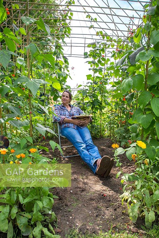 Woman relaxing in the Bean house with a harvest of Runner Bean 'Wisley Magic'. 