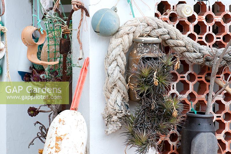 Succulents in recycled containers in a Mediterranean seaside summer garden with old fishing floats and rope 