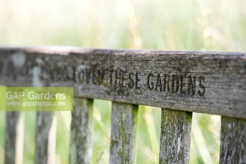 The words Loved These Gardens carved into a memorial wooden garden bench