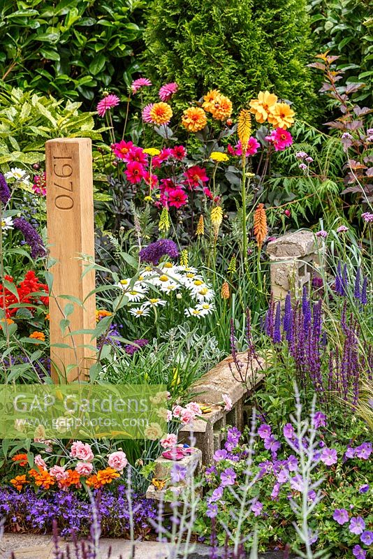 1970s and modern planting including Dianthus 'Doris' and Geranium 'Rozanne' with wooden post marking the eara, The NSPCC Legacy Garden, RHS Hampton Court Flower Show 2014