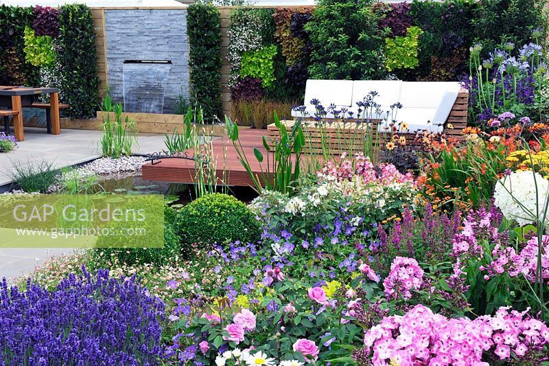 A Hampton Garden. Colourful beds, water feature, raised timber decking area, timber bench