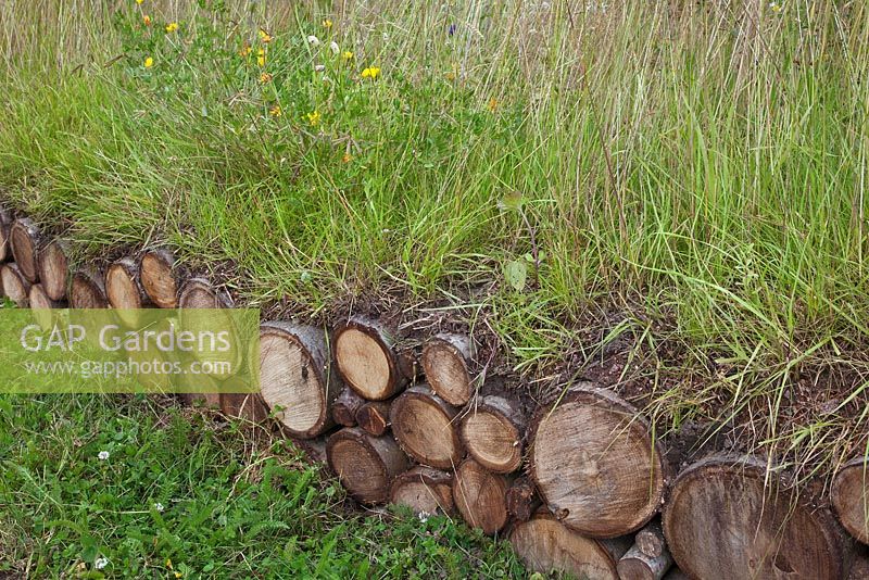 Jordans Wildlife Garden - log pile used as boundary - low wall with grass and flowering plants 