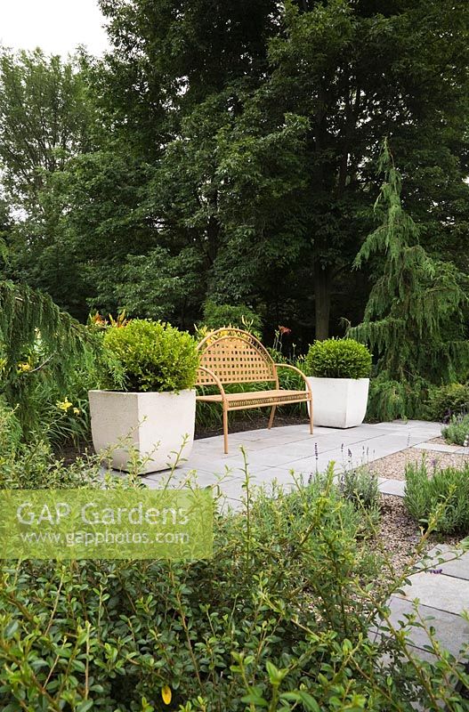 Brown metal lattice garden bench between two cement planters with Box (Buxus 'Green Velvet') shrubs on flagstones  - Il Etait Une Fois garden, Monteregie, Quebec, Canada.