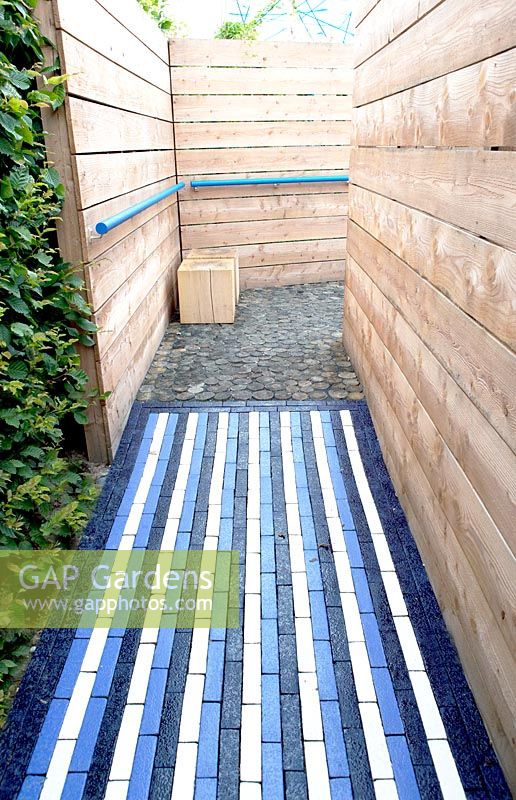 Corridor of wooden fences. Entrance of the garden Synthese is a path of bricks painted in stripes in dark blue, purple and white.
