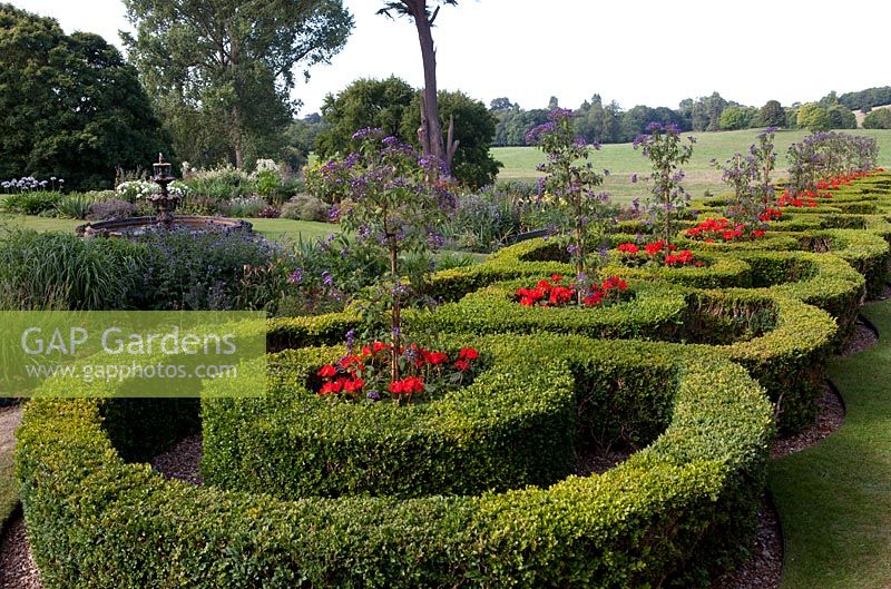 Formal parterre with red pelargoniums, fountain, borders and view to country fields