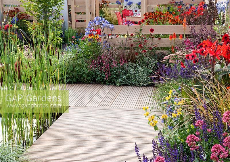 The Narrows - view of decking surrounding pond with bullrushes, mixed borders and oak fence 